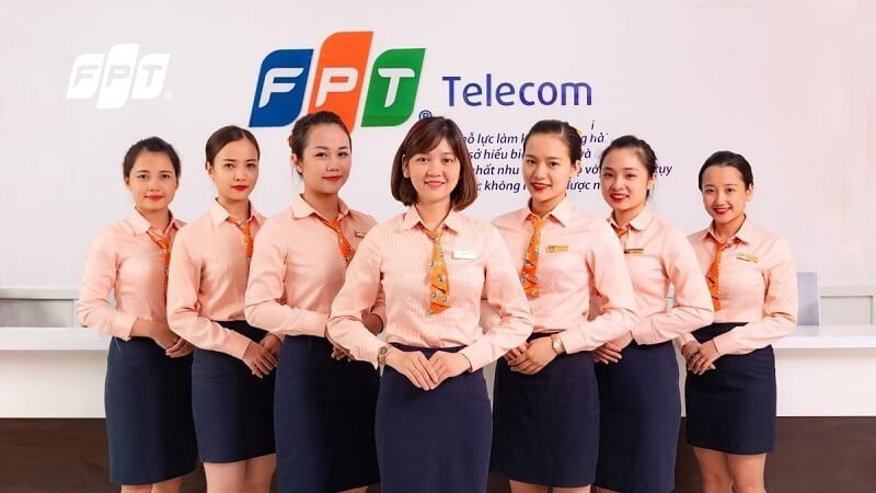 Nhân viên nữ FPT Telecom mặc đồng phục áo sơ mi cam chân váy xanh đứng tại quầy giao dịch